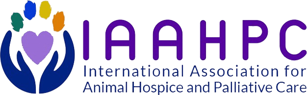 Logo for the International Association for Animal Hospice and Palliative Care. It features two blue hands, like those of a caring veterinarian, holding a purple heart with a paw print above, surrounded by colorful spots. The acronym IAAHPC is in purple.